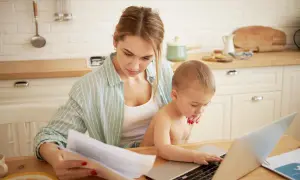 Mama z dzieckiem przy laptopie, analizuje dokumenty. Zastanawia się, urlop rodzicielski ile płatny, by pogodzić pracę i opiekę.