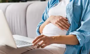 Ciężarna kobieta z laptopem na kolanach, siedząca na kanapie.