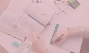 Otwarta książka, ręka pisząca w notatniku, okulary i kalkulator.
