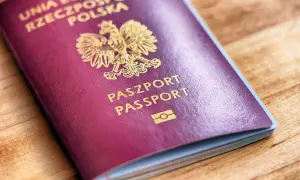 Czerwony paszport z godłem Polski i napisem "PASZPORT" na drewnianym tle.