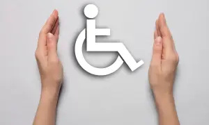 Dwie dłonie otaczają biały symbol osoby na wózku inwalidzkim na jasnoszarym tle.