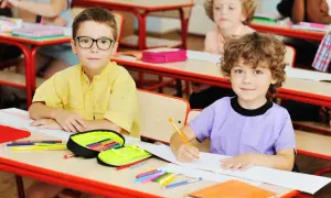 Dzieci w szkole siedzą przy ławkach, rysują i piszą.