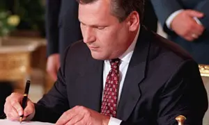 Mężczyzna w garniturze podpisuje dokument piórem.
