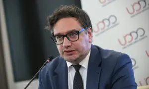 Mężczyzna w okularach i garniturze mówi do mikrofonu na tle logo UODO.