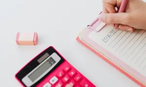 Różowa kalkulatorka, notatnik z zapisanym działaniem matematycznym i gumka do mazania.