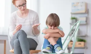 Kobieta w okularach rozmawia ze smutnym chłopcem siedzącym na krześle.
