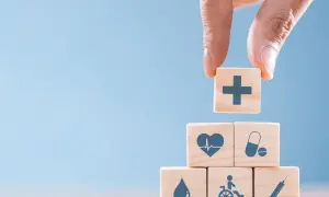 Drewniane klocki z symbolami medycznymi: krzyż, serce, tabletki, kropla, wózek inwalidzki, strzykawka.