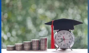 Stos monet, budzik z czapką absolwenta i czerwonym pomponem na tle zieleni.