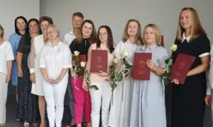Grupa osób pozuje do zdjęcia, trzymając dyplomy i róże.