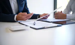 Dwóch mężczyzn omawia dokumenty. Jeden z nich trzyma papier, który może dotyczyć rozwiązania umowy o pracę bez wypowiedzenia.