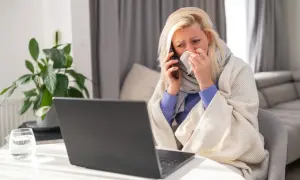 Chora kobieta owinięta kocem rozmawia przez telefon, trzymając chusteczkę.
