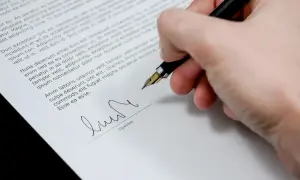 Dłoń podpisuje dokument, być może wypowiedzenie zmieniające warunki umowy.