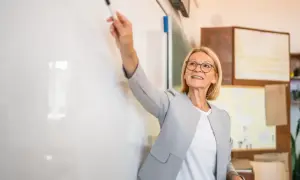Nauczycielka z markerem przy tablicy, uśmiechnięta. To może być ocena pracy nauczyciela początkującego podczas lekcji.