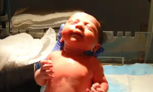 Noworodek w rękach osoby w niebieskich rękawiczkach, na tle białych ręczników.