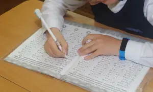 Dziecko pisze długopisem w zeszycie z zadaniami matematycznymi.