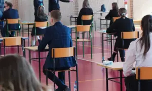 Uczniowie siedzą przy ławkach w sali gimnastycznej podczas egzaminu.