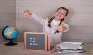 Uśmiechnięta dziewczyna z warkoczami wskazuje palcami na tabliczkę "Back to School" obok globusa i stosu książek.