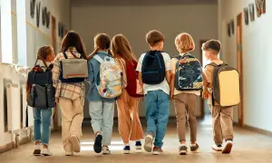 Grupa dzieci z plecakami idzie korytarzem szkolnym. Wszyscy wyglądają na podekscytowanych, jakby to był dzień, kiedy wolne od szkoły.