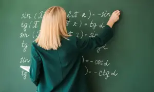 Nauczycielka pisze wzory matematyczne kredą na zielonej tablicy.