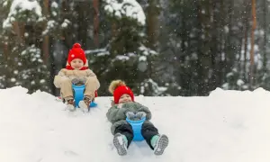 Dzieci zjeżdżają na sankach po ośnieżonym stoku w lesie.