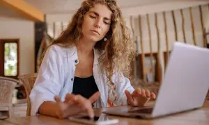 Kobieta z kręconymi włosami pracuje na laptopie i telefonie.