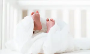 Stópki noworodka owinięte w biały kocyk na tle łóżeczka.