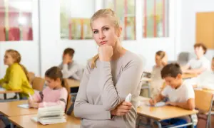 Nauczycielka zamyślona w klasie, gdzie uczniowie piszą. Czy to znak, że godziny ponadwymiarowe nauczycieli są nieuniknione?