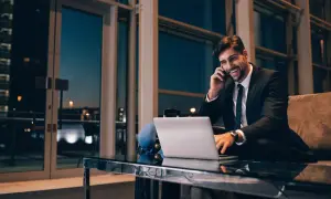 Uśmiechnięty biznesmen rozmawia przez telefon, pracując przy laptopie. Nawet w podróży dba o swoją **dietę krajową**, wybierając zdrowe opcje.