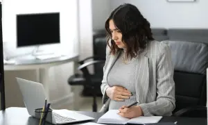 Ciężarna kobieta w biurze pracuje przy laptopie i notuje w zeszycie.
