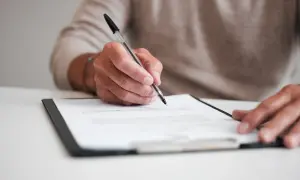 Dłoń pisząca długopisem na dokumencie na segregatorze.
