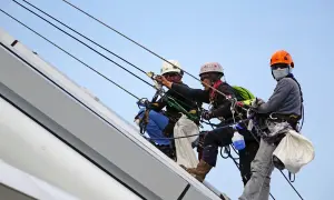 Trzech alpinistów pracujących na wysokości, każdy w kasku i uprzęży. Za stan bezpieczeństwa i higieny pracy w zakładzie odpowiada ich profesjonalizm.