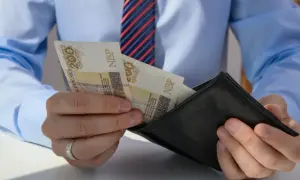 Mężczyzna w koszuli i krawacie wkłada polskie banknoty 200 zł do czarnego portfela.
