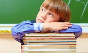 Chłopiec w niebieskiej koszuli opiera głowę na stosie książek, patrząc w górę.