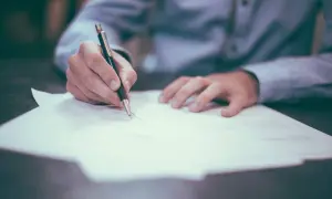 Dłoń pisząca długopisem na papierze.