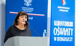 Kobieta przemawia przy mównicy. Dowiadujemy się, jak napisać wniosek o nagrodę kuratora oświaty.