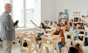 Nauczyciel w klasie, uczniowie podnoszą ręce.