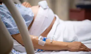 Kobieta w szpitalnym łóżku, z wenflonem w ręce, przechodzi trudny czas urlopu macierzyńskiego po poronieniu.