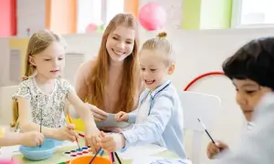 Nauczycielka z dziećmi maluje farbami przy stole w przedszkolu.