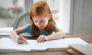 Ruda dziewczynka rysuje przy stole. Czy nauczanie indywidualne może odbywać się zdalnie? Tak, nawet w domu.