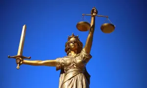 Złota statua Temidy z mieczem i wagą na tle błękitnego nieba.