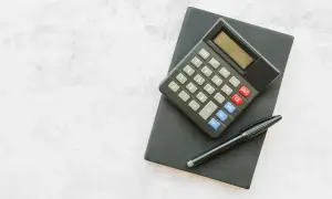 Czarny notatnik z kalkulatorem i długopisem na jasnym tle.
