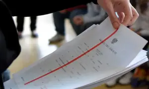 Dłoń trzyma stos świadectw szkolnych z czerwoną linią.