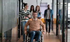 Uśmiechnięty mężczyzna na wózku inwalidzkim w biurze, z kolegami w tle.