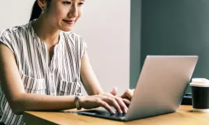Kobieta z uśmiechem pracuje na laptopie, realizując przygotowanie pedagogiczne online.