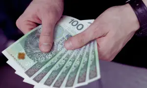 Dłonie trzymają stos banknotów 100 zł. To może być wynagrodzenie młodocianych za ich pierwszą pracę.