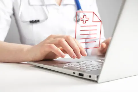 Lekarz wpisuje dane pacjenta na laptopie, dbając o zgodność z oryginałem dokumentacji medycznej.