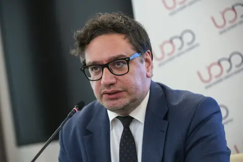 Mężczyzna w okularach i garniturze mówi do mikrofonu na tle logo UODO.