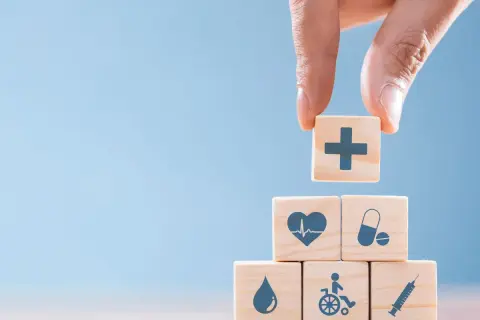 Drewniane klocki z symbolami medycznymi: krzyż, serce, tabletki, kropla, wózek inwalidzki, strzykawka.