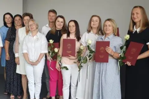 Grupa osób pozuje do zdjęcia, trzymając dyplomy i róże.