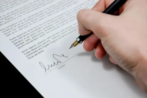 Dłoń podpisuje dokument, być może wypowiedzenie zmieniające warunki umowy.